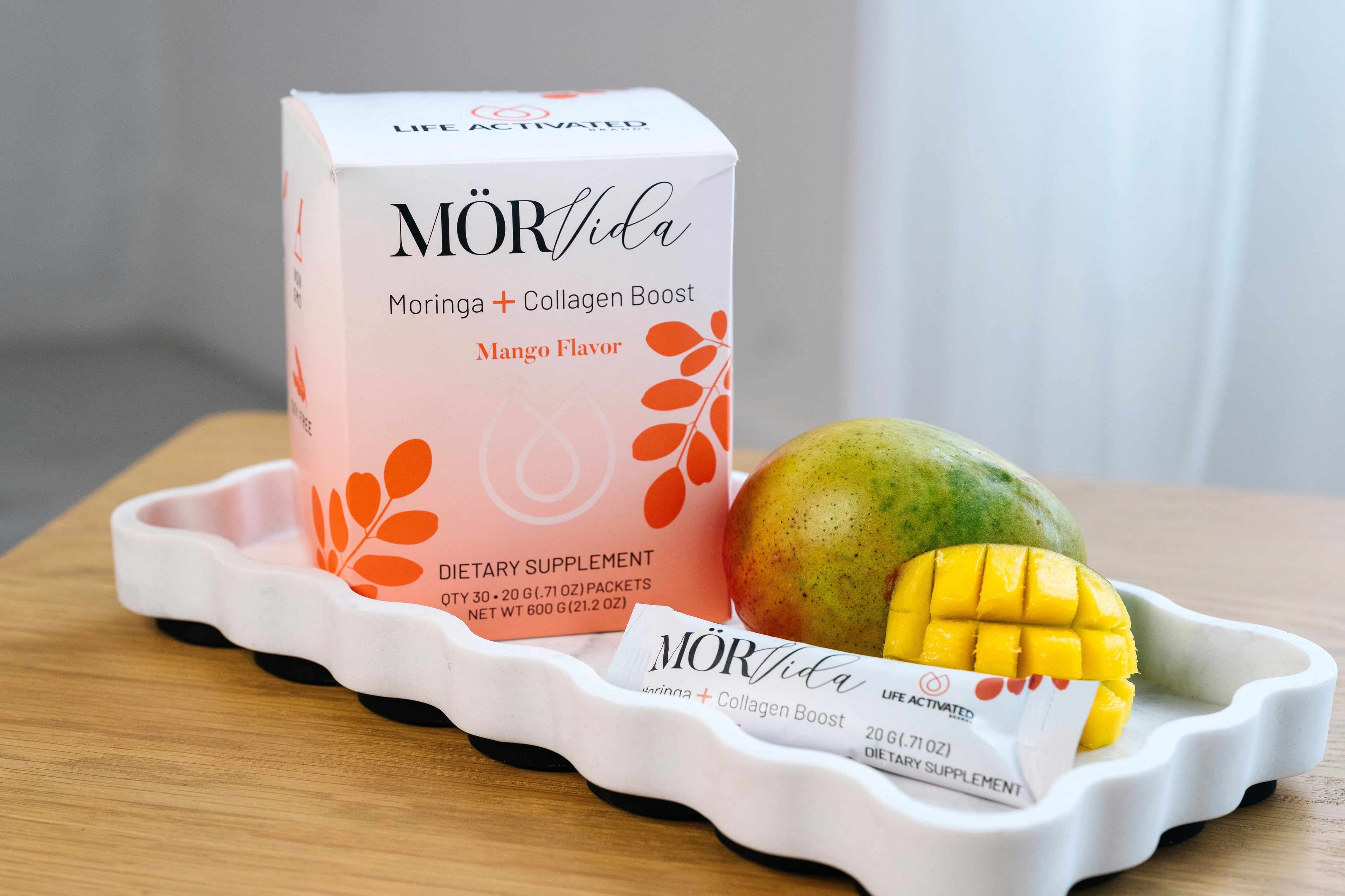 Morvida Moringa + Collagen Boost supplement packaging with a mango on a white tray.